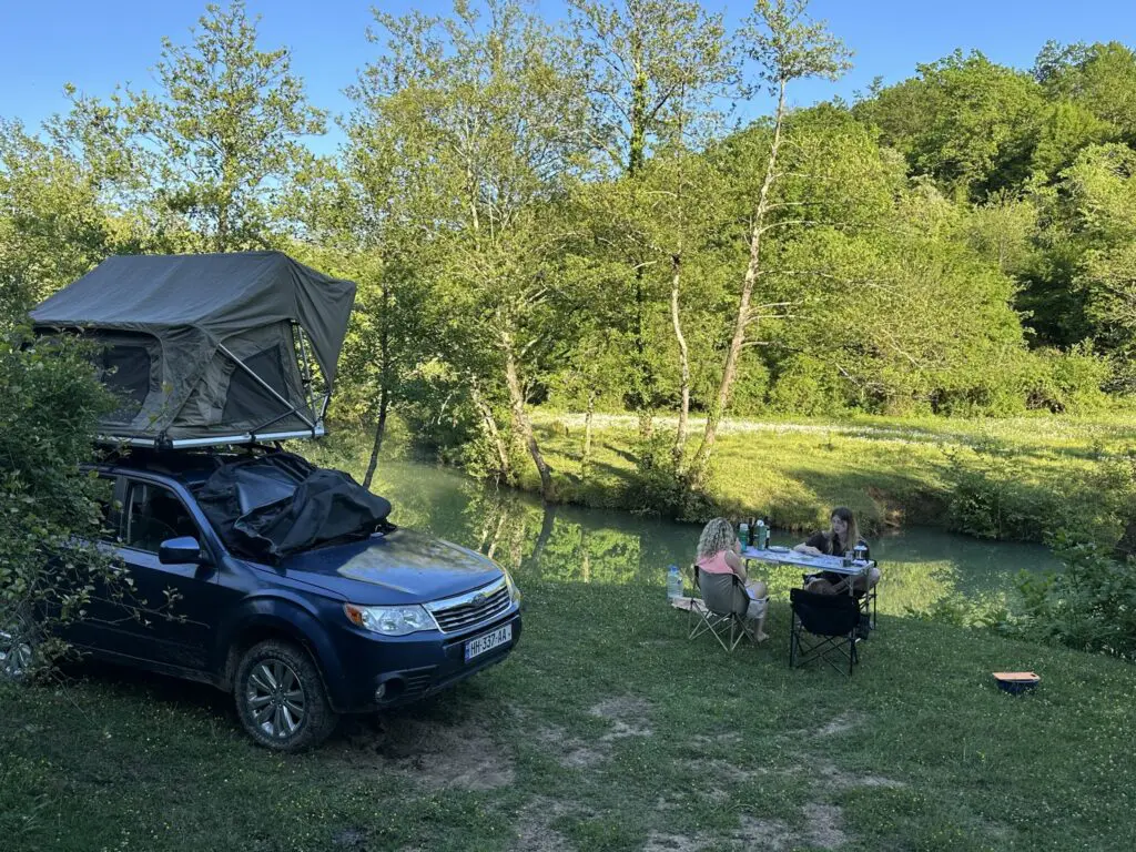 two women camping by a river with a rooftop tent car