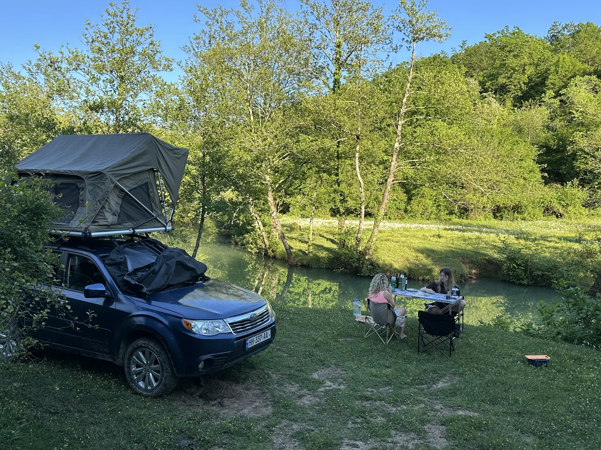 two women camping by a river with a rooftop tent car