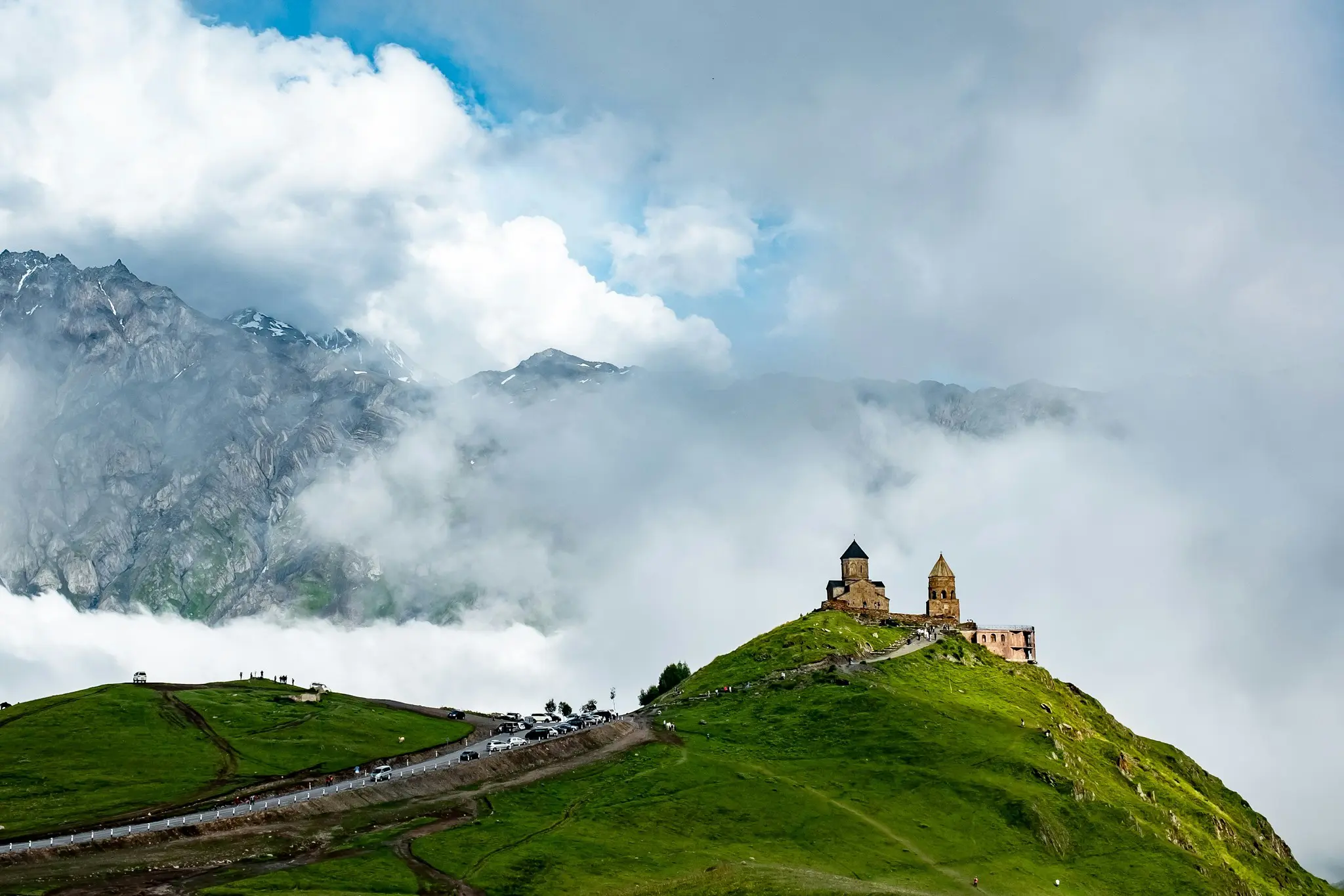 Gergeti Trinity Church on a green hill with mountains and clouds