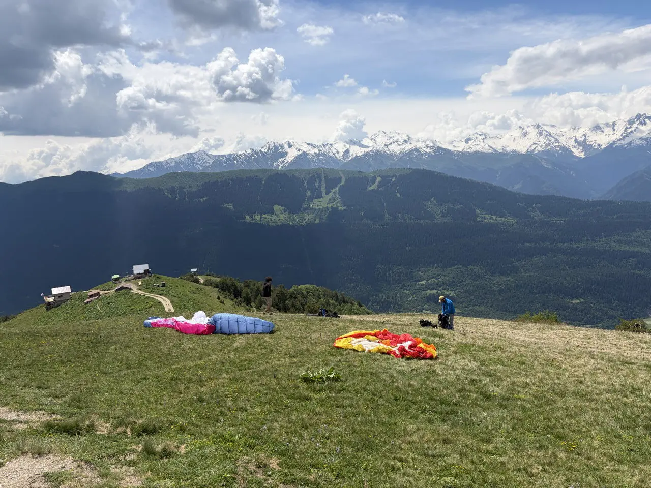 paragliders preparing on a mountain ridge with snowy peaks