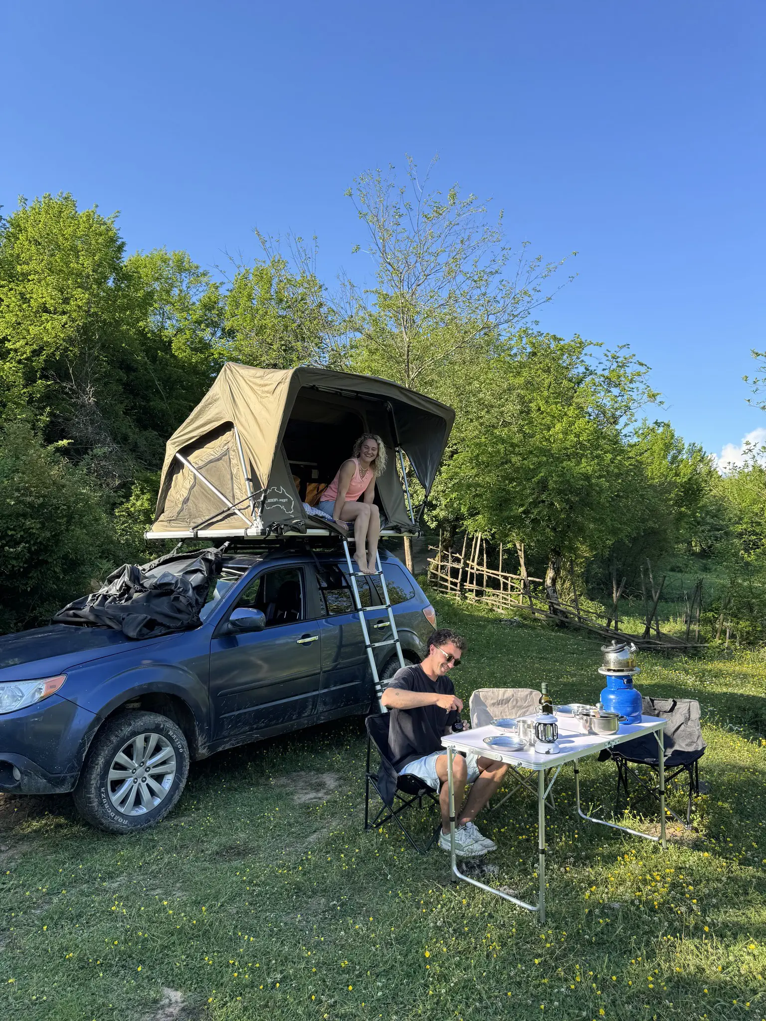 couple camping with rooftop tent and outdoor cooking setup