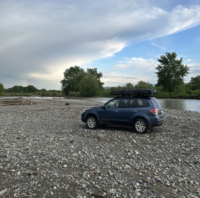 blue subaru with rooftop tent parked by a rocky river