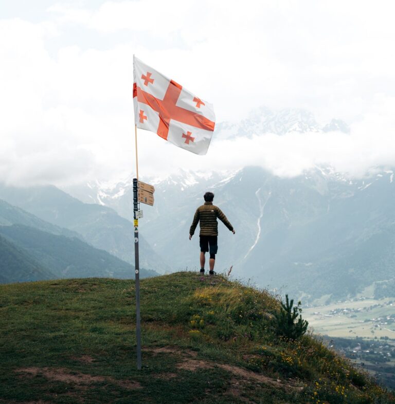 hiker on a mountain ridge with Georgia flag and snowy peaks